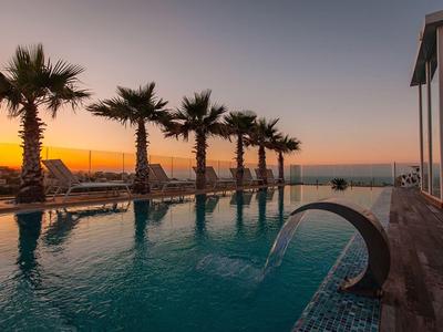 Piscina dell'hotel con palme e vista sul mare al tramonto