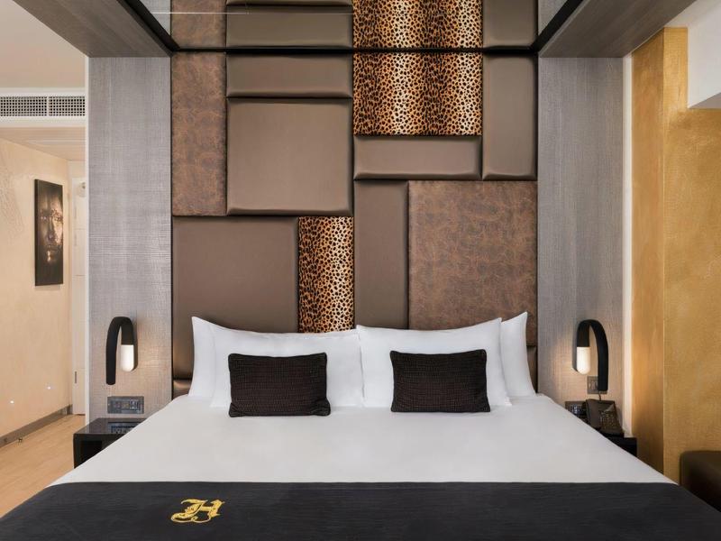 Nowoczesny pokój hotelowy z dużym łóżkiem, dekoracyjnym panelem ściennym i stylowymi lampkami do czytania.