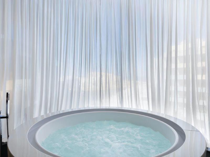 Okrągłe jacuzzi z bąbelkującą wodą przed przezroczystą białą zasłoną.