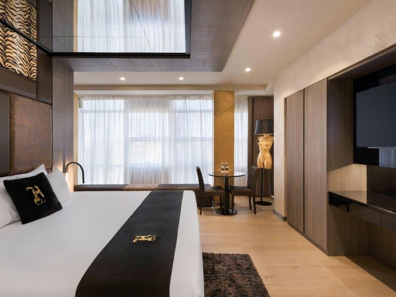 Nowoczesny pokój hotelowy z dużym łóżkiem, biurkiem i dużym oknem z zasłonami.