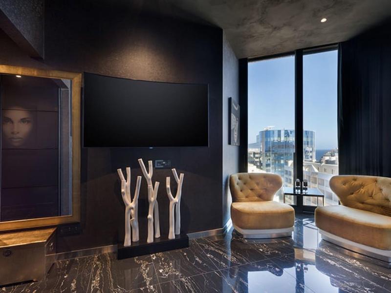 Elegancki salon z dwoma złotymi fotelami, dużym oknem i nowoczesną sztuką na czarnej ścianie.