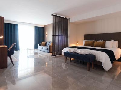 Jasny pokój hotelowy z dużym łóżkiem, sofą, biurkiem i marmurową podłogą.