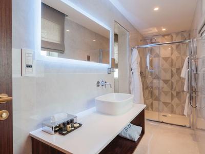 Moderní, světlá koupelna s umyvadlem, oválným zrcadlem a skleněným sprchovým koutem.