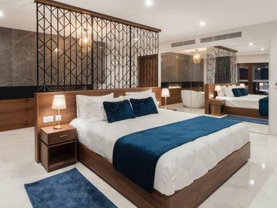 Moderní hotelový pokoj s velkou postelí, modrými akcenty a dekorativní příčkou.