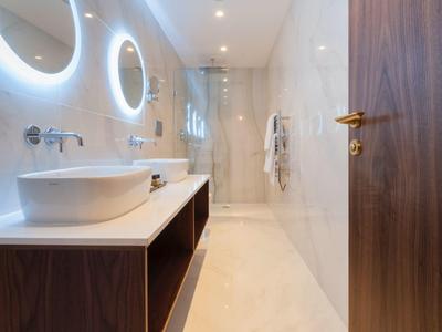 Moderní koupelna se dvěma kulatými osvětlenými zrcadly a sprchou na pravé straně.