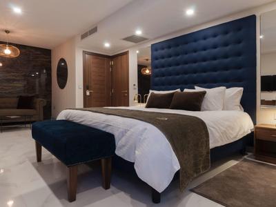 Moderní hotelový pokoj s velkou modrou postelí, lavičkou a teplým osvětlením.