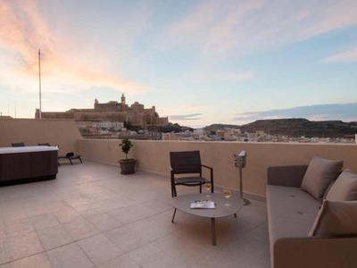 Střešní terasa s posezením a vířivkou s výhledem na město a kopce při západu slunce.