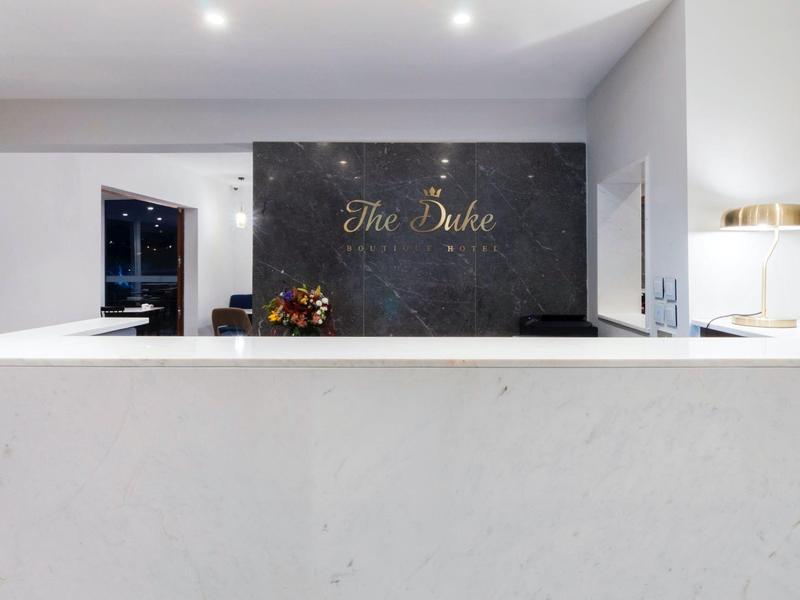 Moderní bílá recepce s černou stěnou a zlatým nápisem 'The Duke'.