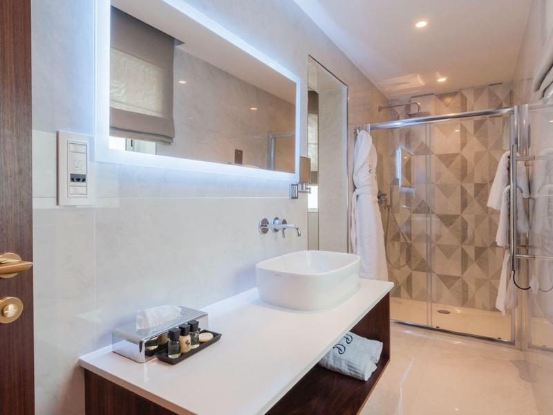 Moderní, světlá koupelna s umyvadlem, oválným zrcadlem a skleněným sprchovým koutem.