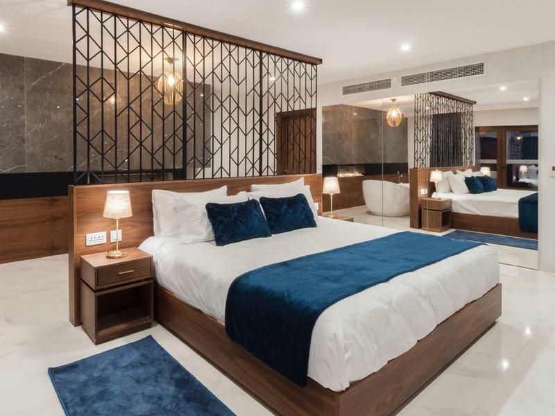 Moderní hotelový pokoj s velkou postelí, modrými akcenty a dekorativní příčkou.