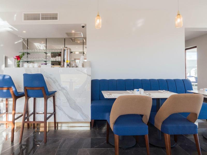 Moderní restaurace s modrými židlemi, barem a bílou stěnou