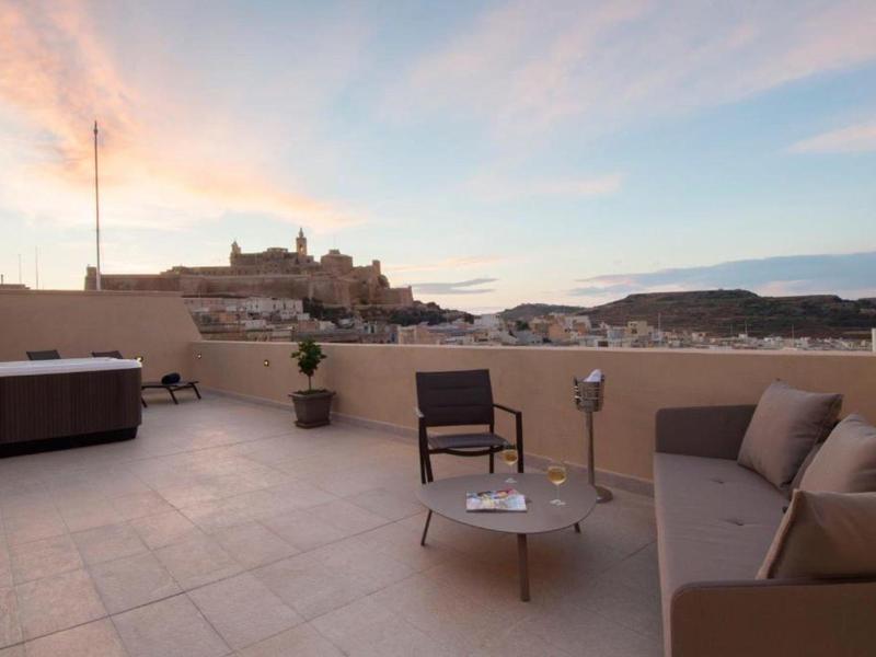 Střešní terasa s posezením a vířivkou s výhledem na město a kopce při západu slunce.