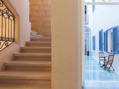 Escalier avec rampe décorative à gauche et volets bleus à droite.