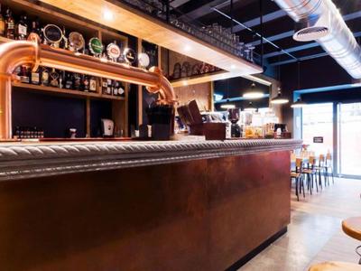 Bar moderne avec comptoir en bois, robinets en cuivre et éclairage chaleureux.