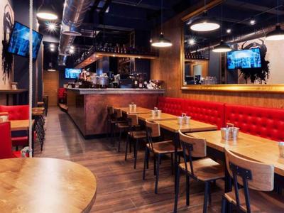 Intérieur de restaurant moderne avec des banquettes rouges, des tables en bois et un sol foncé.