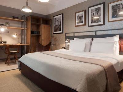 Nowoczesny pokój hotelowy z dużym łóżkiem, biurkiem i obrazami na ścianie.