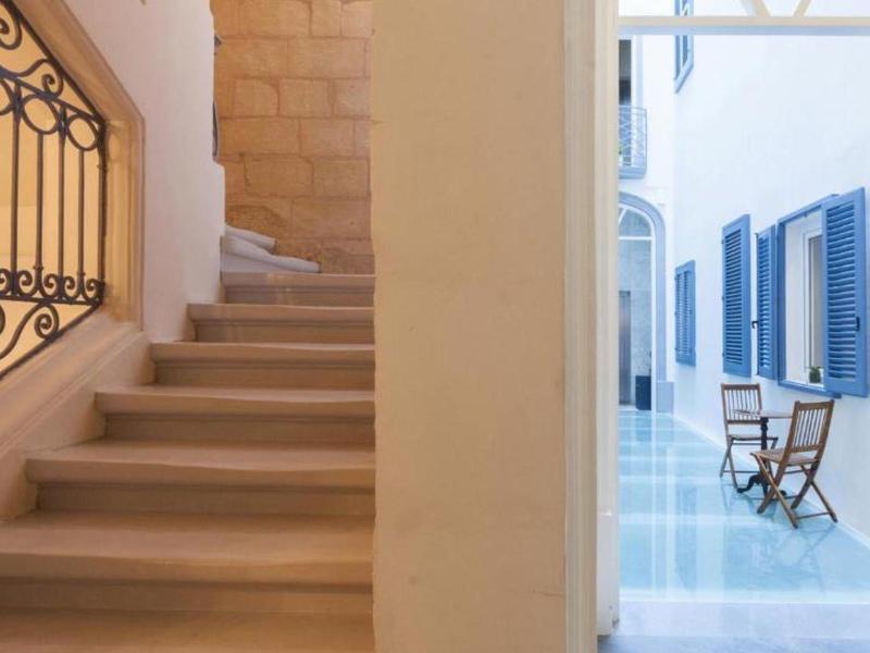 Schody i jasny korytarz z niebieskimi okiennicami i krzesłem przy ścianie.