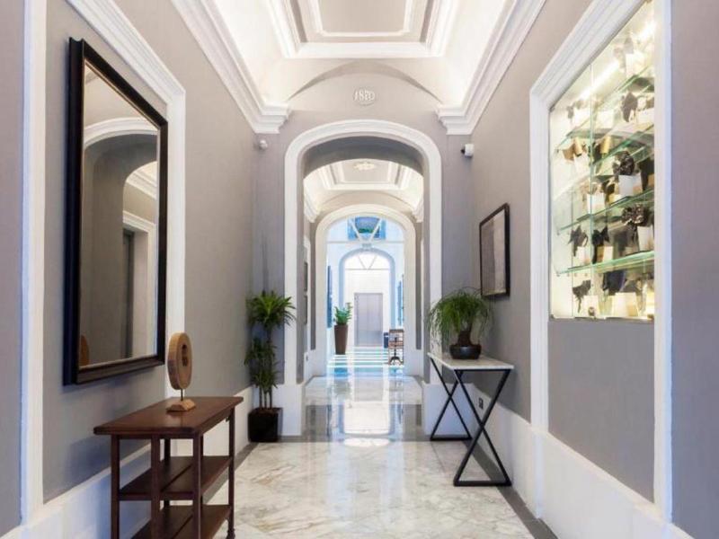 Jasny korytarz hotelowy z marmurową podłogą, stylowymi meblami i wysokim sufitem z listwami.