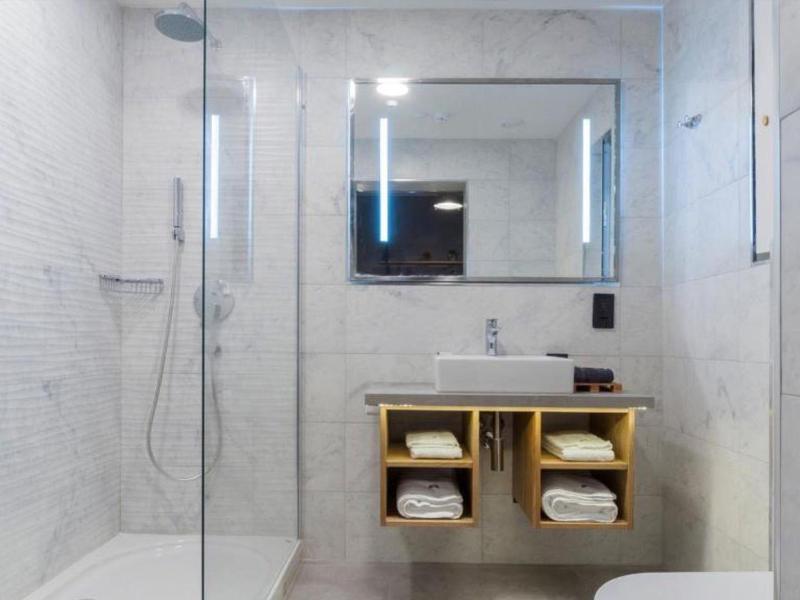 Nowoczesna łazienka z prysznicem typu walk-in, dużym podświetlanym lustrem i otwartą półką na ręczniki.