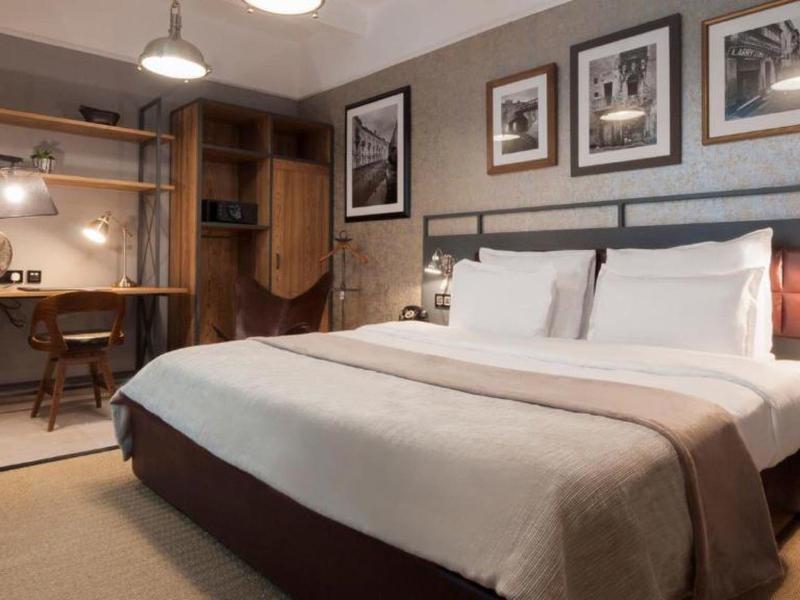 Nowoczesny pokój hotelowy z dużym łóżkiem, biurkiem i obrazami na ścianie.