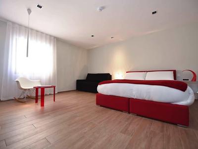 Modern eingerichtetes Hotelzimmer mit rotem Bett, schwarzem Sofa und großem Fenster.