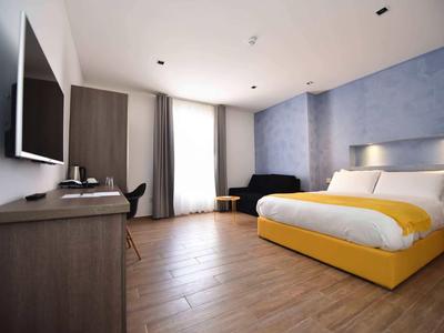 Modernes Hotelzimmer mit Doppelbett und Holzboden, grauen Wänden und großen Vorhängen.