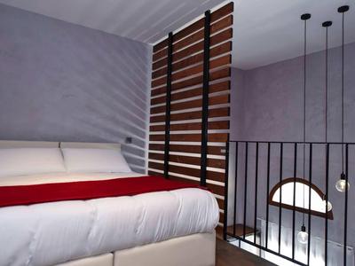 Modernes Hotelzimmer mit hellem Bett, roter Decke und Holzlattenwand neben Treppe.