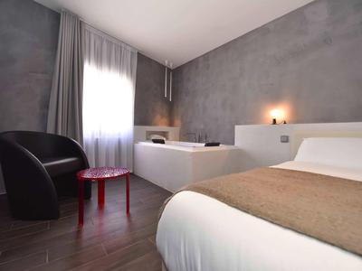 Modernes Hotelzimmer mit grauen Wänden, Doppelbett, Sessel und rotem Beistelltisch.