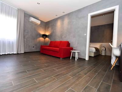 Modernes Hotelzimmer mit rotem Sofa, grauen Wänden und dunkelbraunem Holzboden.