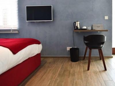 Modernes Hotelzimmer mit rotem Bett, grauer Wand, TV und kleinem Schreibtisch mit Stuhl.