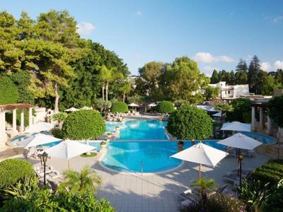 Großer blauer Pool mit weißen Sonnenschirmen, umgeben von grünen Bäumen und Gebäuden.