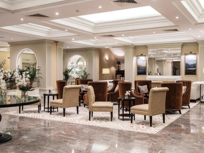 Heller, eleganter Hotel-Lobbybereich mit Stühlen, Tischen, großen Spiegeln und Blumenarrangements.