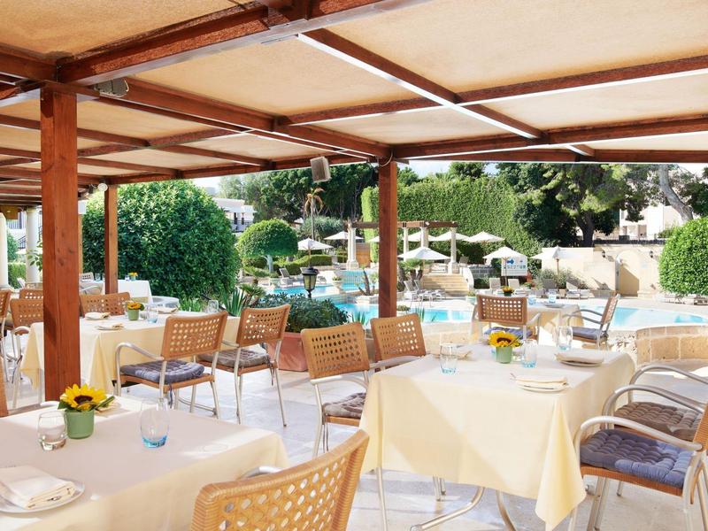 Freiluftrestaurant mit gedeckten Tischen, geflochtenen Stühlen und Blick auf Pool und Grünflächen.