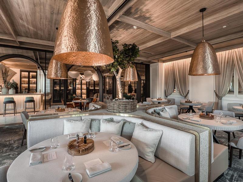 Elegantes Restaurant mit runden Tischen, bequemen Sitzbänken und großen kupfernen Lampen.