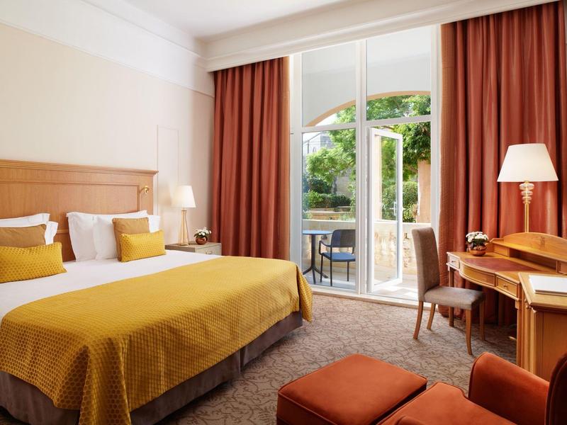 Hell eingerichtetes Hotelzimmer mit Doppelbett, gelben Akzenten, Schreibtisch und Balkonzugang.