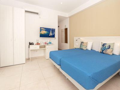 Modernes Schlafzimmer mit zwei Betten, kleinem Schreibtisch, Fernseher und weißem Kleiderschrank.