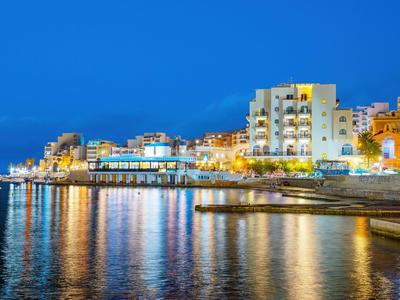 Abendliche Hafenansicht mit beleuchteten Gebäuden und Wasserreflexionen bei klarem Himmel.
