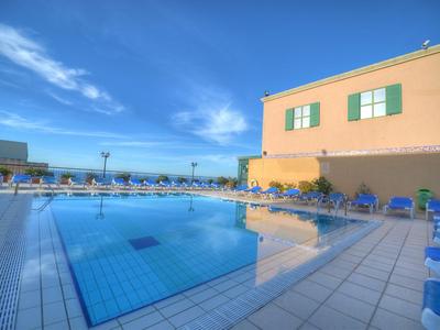 Hotelpool mit blauen Liegestühlen und Sonnenschirmen unter hellem Himmel.
