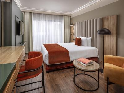 Modernes Hotelzimmer mit Doppelbett, orangenen Akzenten und einem kleinen Sitzbereich.