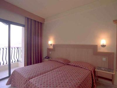 Hotelzimmer mit zwei Einzelbetten, braunen Bettdecken und Balkon mit Geländer.