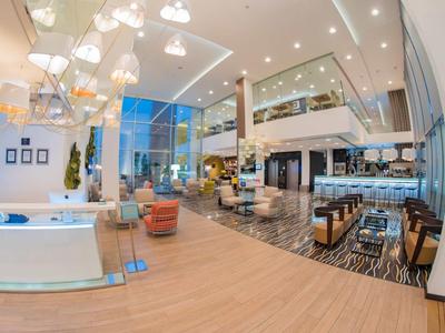Großer heller Hotel-Lobbyraum mit modernen Möbeln, Holz- und Marmorboden, Glasfront und hoher Decke.
