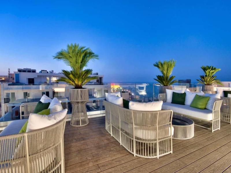 Taras na dachu z białymi meblami, roślinami i widokiem na miasto o zmierzchu.