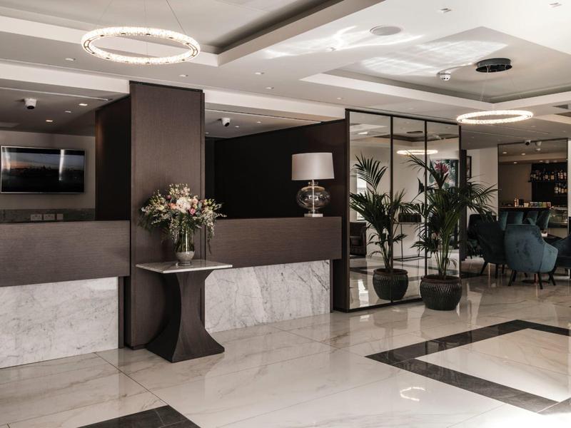 Modern hotel lobby with marble floors, plants, seating area, and elegant lighting.