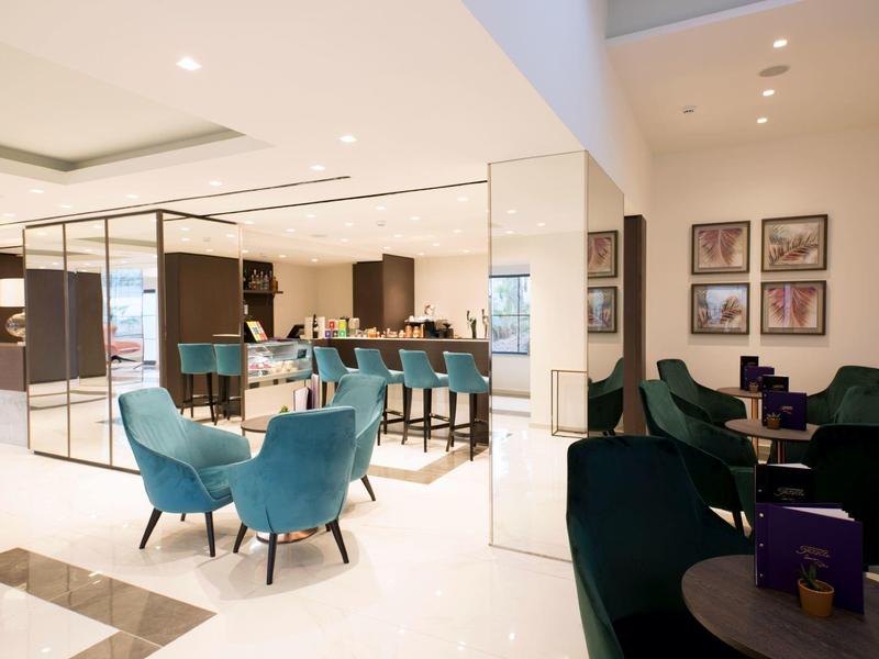 Modern hotel lobby with turquoise chairs, bar area, and framed artwork on walls.