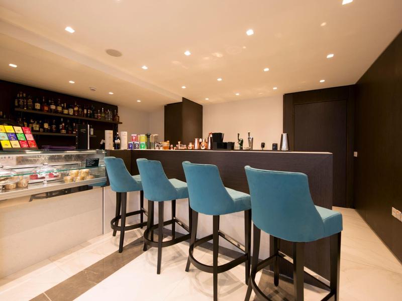 Modern hotel bar with blue bar stools and illuminated shelves under warm lighting.