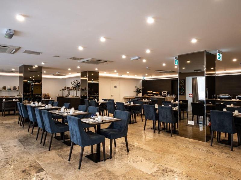 Spacious hotel dining room with blue chairs, black tables, and marble flooring under bright lights.