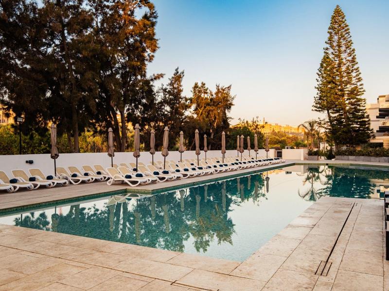 Outdoor hotel pool with lounge chairs under a clear sky during sunset.