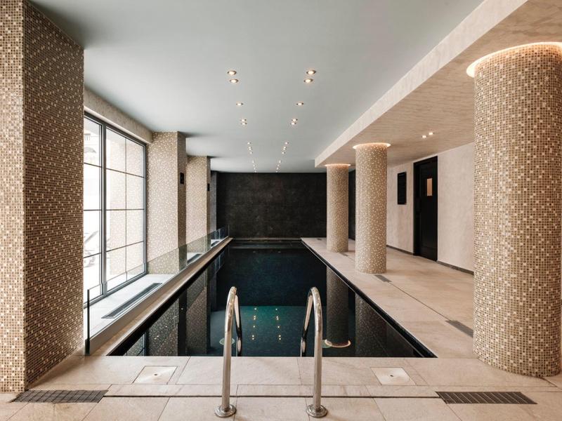 Indoor hotel pool with beige pillars and large windows letting in natural light.
