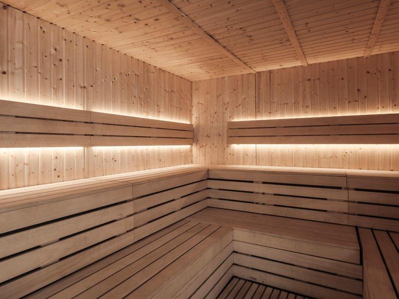 Cozy wooden sauna with tiered benches and warm, recessed lighting along the walls.
