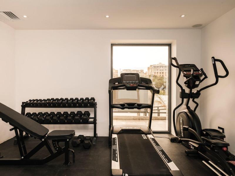 Modern gym with treadmill, dumbbells, adjustable bench, and elliptical trainer under bright lights.